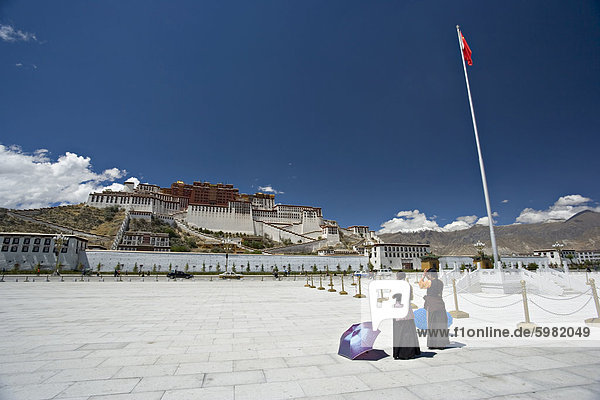 Zwei tibetische Frauen beten  vor dem Potala-Palast  UNESCO-Weltkulturerbe  mit chinesischen Flagge auf der rechten Seite  Lhasa  Tibet  China  Asien