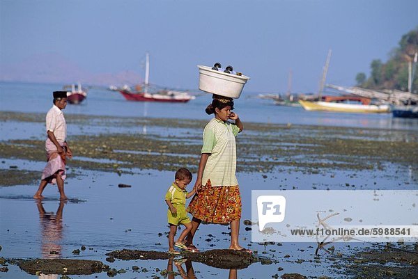 Mutter und Kind gehen bei Ebbe aus dem Port Labuhanbajo  im Westen der Insel Flores  Indonesien  Südostasien  Asien