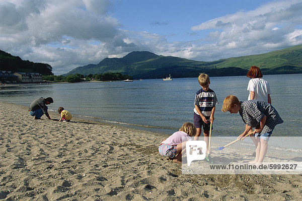 A small group of children digging on the beach by the lake  Loch Lomond  Trossachs  Scotland  United Kingdom  Europe