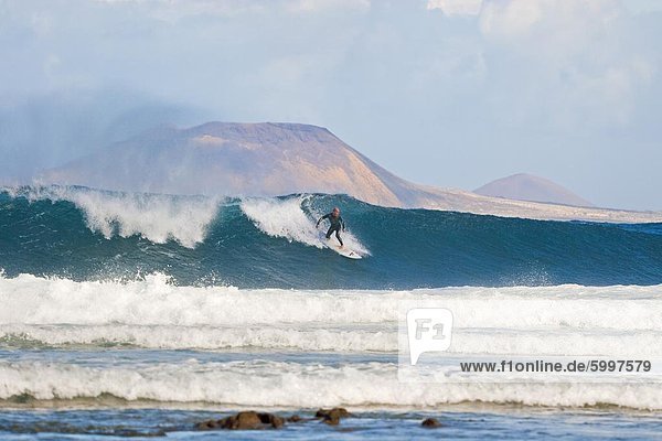Surfer on a large wave with Graciosa Island beyond  at the world class surf reef break known as San Juan  east of Famara in the north of the island  Famara  Lanzarote  Canary Islands  Spain  Atlantic  Europe