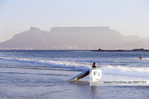Junge Frau Surfer tritt das Wasser des Atlantischen Ozeans mit Tafelberg im Hintergrund Kapstadt Südafrika Afrika