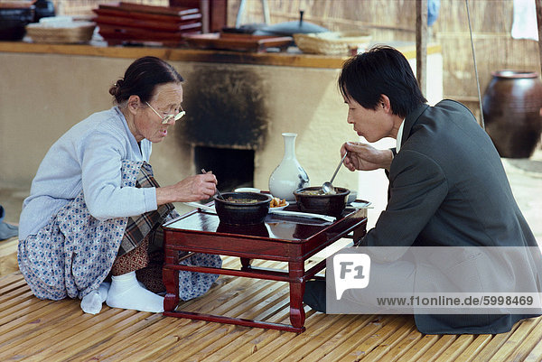 Two people eating food from a low table in the restaurant area of Folk Village in South Korea  Asia