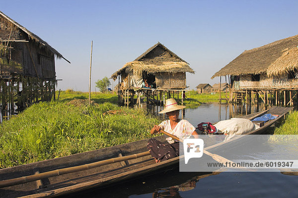 Woman in canoe paddles past floating village  Inle Lake  Shan State  Myanmar (Burma)  Asia