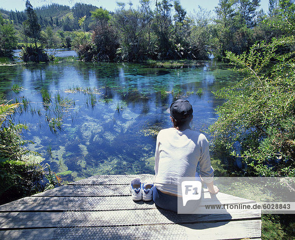 A tourist sitting on the edge of Pupu springs  largest freshwater spring in New Zealand  at Golden Bay  South Island  New Zealand  Pacific