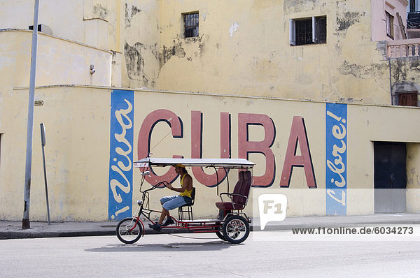 Eine Rikscha übergeben ein Wand-Zeichen feiert kubanischen Freiheit  Havanna  Kuba  Westindische Inseln  Mittelamerika