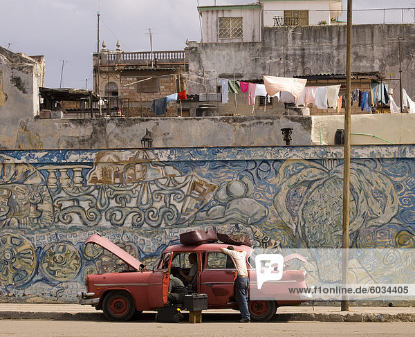 Zwei Männer reparieren ein altes Auto geparkt vor eine bunte Wandbild im zentralen Havanna  Kuba  Westindische Inseln  Mittelamerika