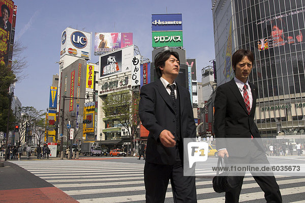 Gut gekleidet zwei junge Männer gehen auf Zebrastreifen mit Werbeplakaten und riesigen video-Bildschirm im Hintergrund  Shibuya  Tokyo  Honshu  Japan  Asien