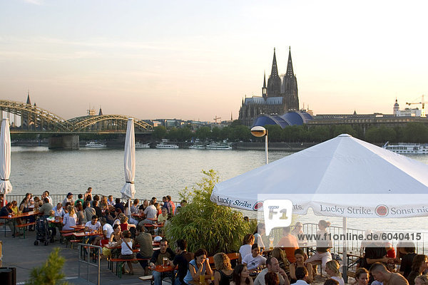 Menschen an trendigen Rheinterrassen Bar und Restaurant neben den Rhein mit der Altstadt und der Kathedrale jenseits,  Köln,  Nord Rhein Westfalen,  Deutschland
