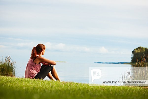 Frau sitzt auf dem Gras Blick auf See