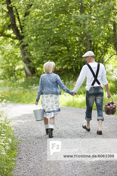 Mature couple holding hands and walking through graveled road