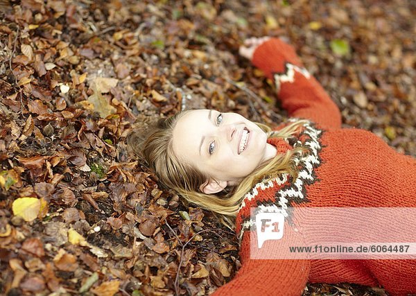 Junge attraktive Frau tragen rote wolligen Jumper auf Boden bedeckt mit Herbstlaub