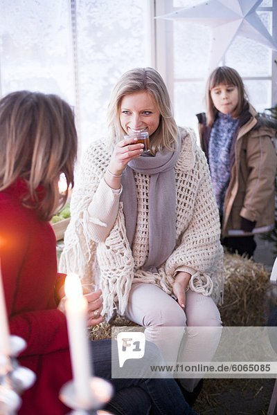 Frau trinkt mit zwei Mädchen in Winterkleidung im Gewächshaus