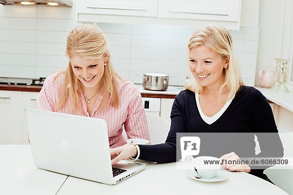 Two young women using laptop in kitchen