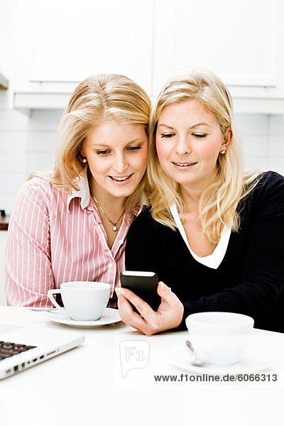 Zwei junge Frauen mit Handy in Küche