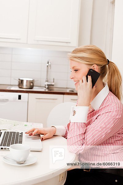 Young woman using laptop and mobile phone in kitchen