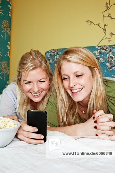 Zwei junge Frauen mit Handy im Schlafzimmer