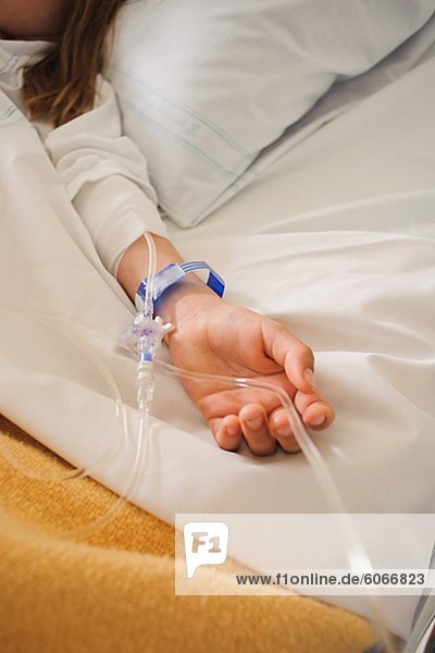 Girl lying on hospital bed with IV drip on arm
