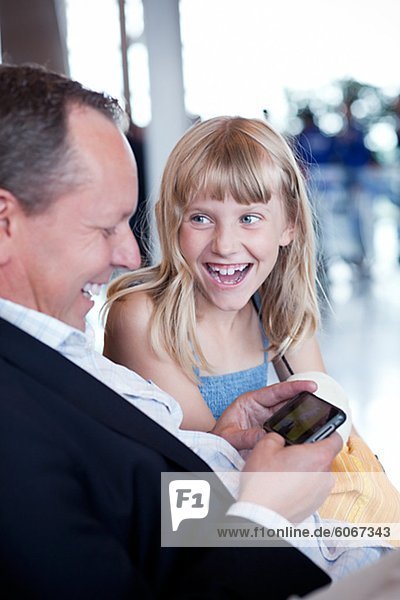 Vater mit Tochter sitzen am Flughafen und am Handy spielen