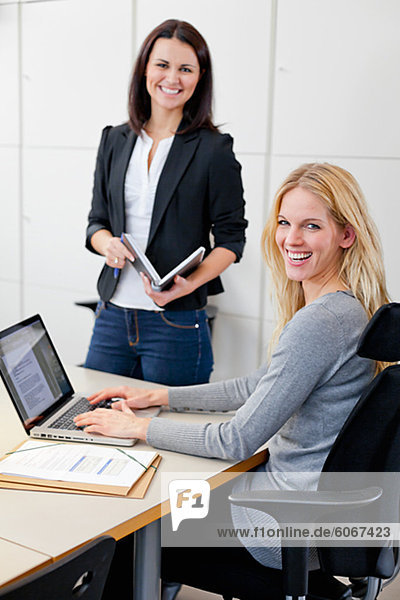 Two female colleagues posing together in office environment