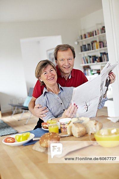 Mature couple reading newspaper during breakfast