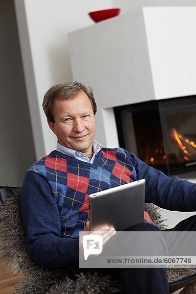 Portrait of mature man sitting by fire place with digital tablet