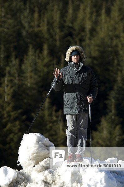 A man on a snowbank after a day of skiing with pines in the background.