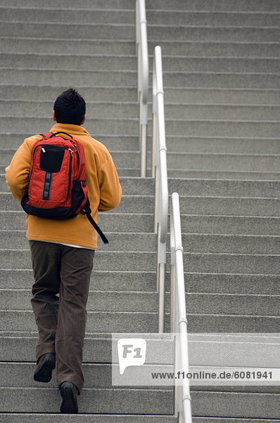 A man going up stairs with a backpack on in an urban environment.