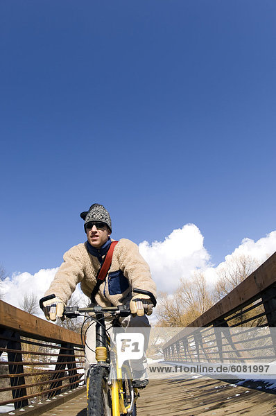 A man rides his bike over a wooden bridge against a blue sky.