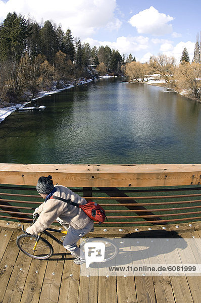 A man rides his bike over a wooden bridge crossing a river.
