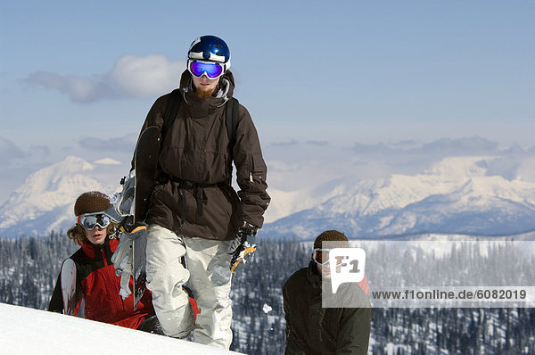 Three young men walk up a snowy mountain with their snowboards in the backcountry.
