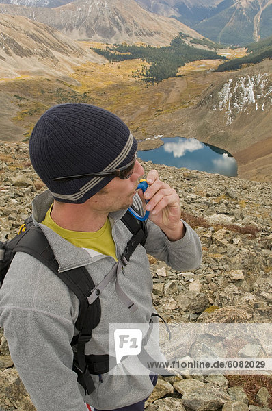 A man stops to hydrate while hiking along an alpine ridge on a crisp fall day.