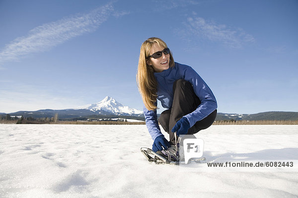 Young woman straps on snowshoes with Mt. Hood  Oregon in background.