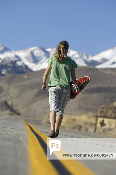 Young woman skateboarding in Bishop  CA with mountains in the background.