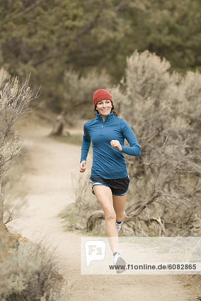 A woman in bright colors jogging on a dirt trail.