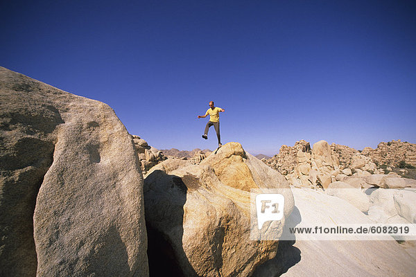 Male hiker leaps from a boulder.