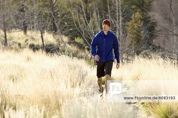 A man in a blue jacket walks along a trail at in Oregon  while in the foreground yellow grass waves in the breeze.