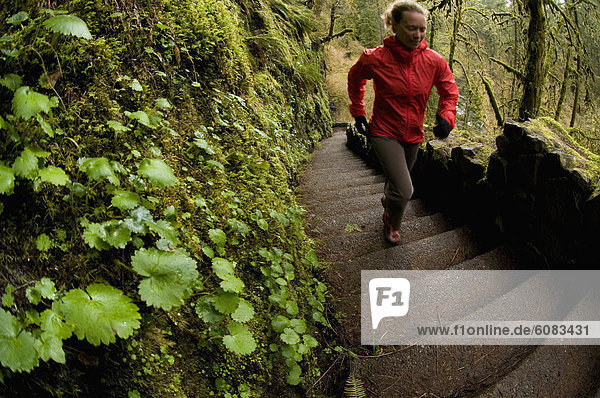 A woman trail running up stairs through a green  mossy forest in Silver Falls State Park  Oregon  USA.