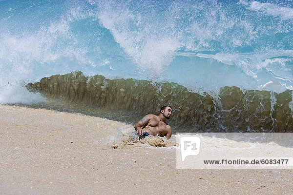 A young man about to be hit by wave at Keiki Beach on the North Shore of Oahu  Hawaii.