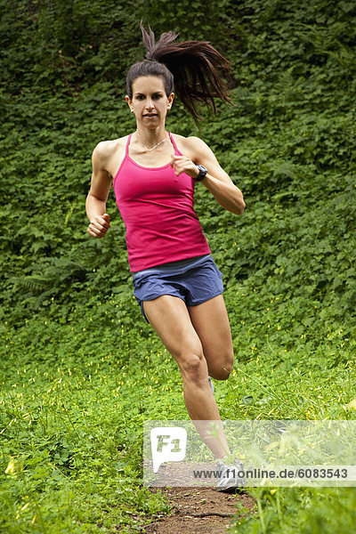Woman trail running through a green meadow in the woods.
