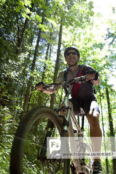 A mountain biker smiles while riding a narrow path through a lush green forest.