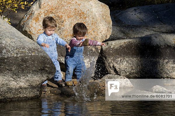 Twin toddlers  a brother and sister  throwing rocks in a stream.