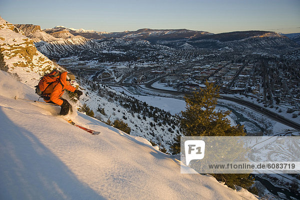 A teenage boy skiing at sunrise down a snowy slope above the town of Durango  Colorado.