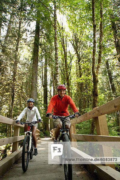 Two mountain bikers riding over a wooden bridge in a forest.