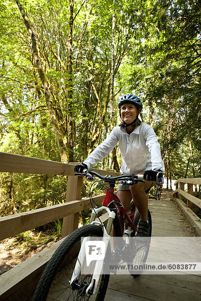A woman riding her mountain bike across a wood bridge.