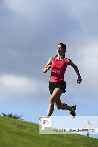 An athletic woman running along the crest of a hill in San Diego  California.