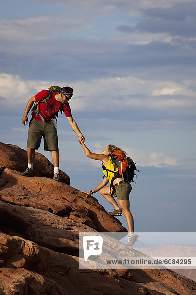 A man reaching down and helping a woman up a rock step in Arches National Park  Utah.