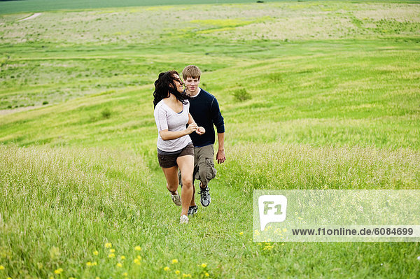 Young couple running up a hill through a bright green field at Spirit Mound  South Dakota.
