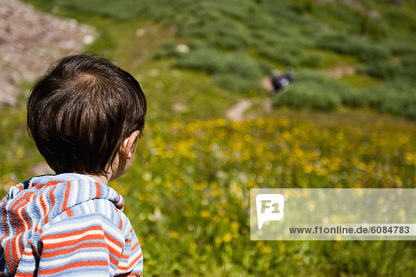 A 14 month old boy gazes out while playing in a meadow while on a multiday backpacking trip in the Maroon Bells in Snowmass Wilderness outside of Aspen.