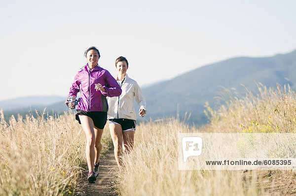 Two young women trail running in the mountains on an early morning.