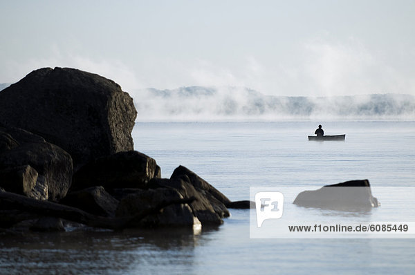 Man fishing in canoe on a misty Lake Sebago  Maine.
